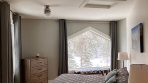 Un dormitorio con una cama grande, un aparador, una ventana con vistas a árboles y una lámpara en el techo.