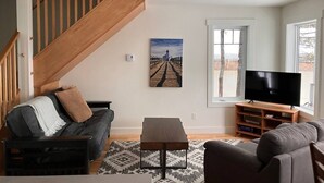 Una sala de estar moderna con una escalera, un televisor de pantalla plana y un cuadro en la pared.