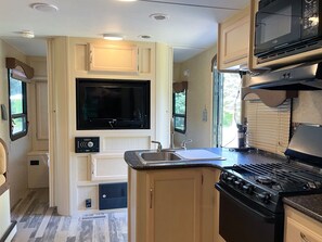 Une cuisine compacte pour camping-car, dotée d’un téléviseur intégré, d’une cuisinière, d’un évier et d’un espace de rangement réduit.