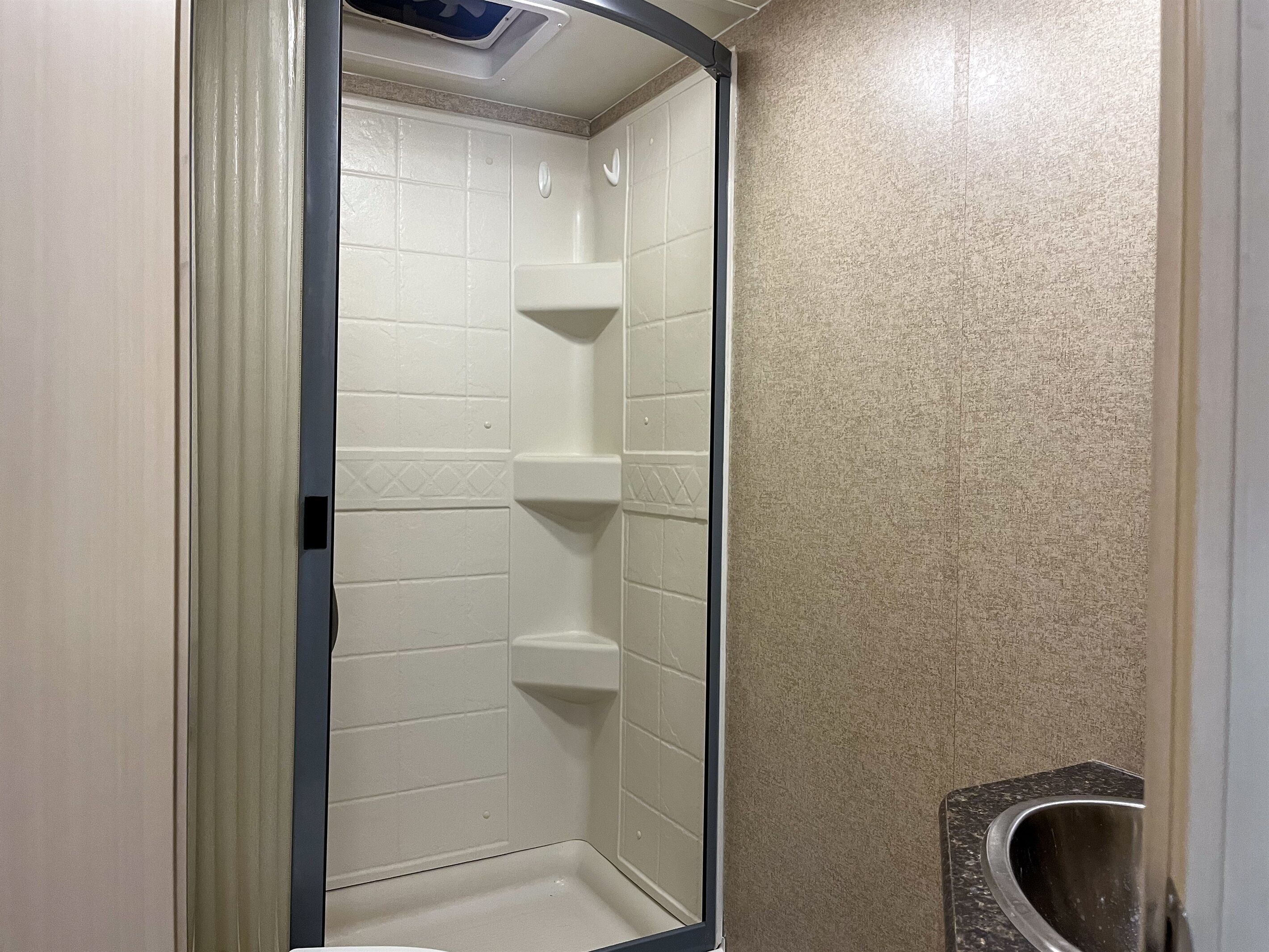 A bathroom with white tiled walls, a shower stall, and a corner sink.