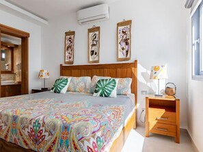 Ein Hotelzimmer mit einem großen Bett, einem hölzernen Kopfteil, einem Nachttisch mit Lampe und Wandbildern über dem Bett.