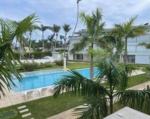 Ein Swimmingpool mit Liegestühlen, umgeben von Palmen und einem gepflegten Rasen.