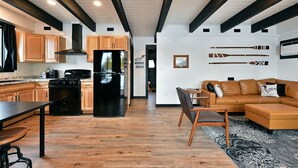 Una cocina moderna con armarios de madera, una estufa negra y un refrigerador. Hay un comedor con una mesa y sillas, y una sala de estar con un sofá y una mesa de centro.