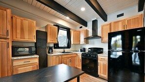 Una cocina moderna con armarios de madera, un refrigerador negro, una estufa y un microondas.