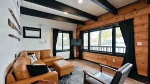 Una sala de estar acogedora con un sofá de cuero, una mesa de centro de madera y un ventanal con cortinas.
