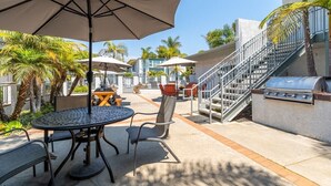 An outdoor patio with a round table, chairs, and umbrellas. There is a grill and a staircase leading to an upper level. - Sandyland Beach Studio Carpinteria (Carpinteria)