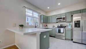 A modern kitchen with a central island, stainless steel appliances, and light green cabinetry. - 4 bedroom fully Fenced 2+ Garage Pkg & Air Cond pet friendly  (Colorado Springs)