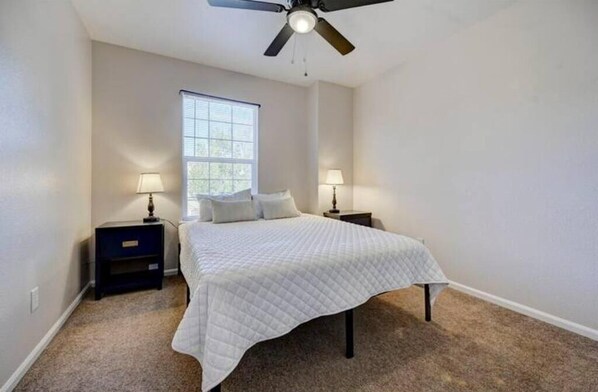 A bedroom with a bed, two bedside tables with lamps, a ceiling fan, and a window.