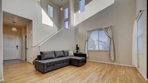 A spacious living area with a large sectional sofa, a staircase, and a large window with curtains. - 4 bedroom fully Fenced 2+ Garage Pkg & Air Cond pet friendly  (Colorado Springs)