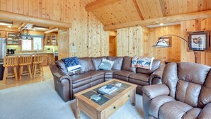 A spacious living room with a brown leather sectional sofa, a glass coffee table, and a wooden ceiling with exposed beams. - Lake & Mtn Views: Spectacular Grand Lake Home (Grand Lake)