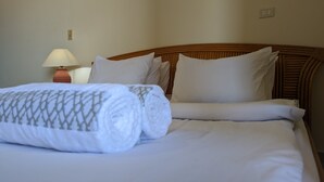 Una cama bien hecha con sábanas blancas y una manta decorativa, un cabecero de madera y una mesita de noche con una lámpara.