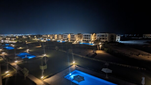 Vista nocturna de un resort con varias piscinas y edificios iluminados.