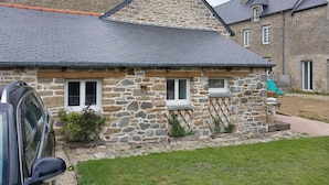 Ein Steinhaus mit einem geneigten Dach, einer kleinen Veranda und einem geparkten Auto davor.