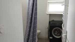 Ein kleines Badezimmer mit Duschvorhang, Toilette und Waschmaschine.