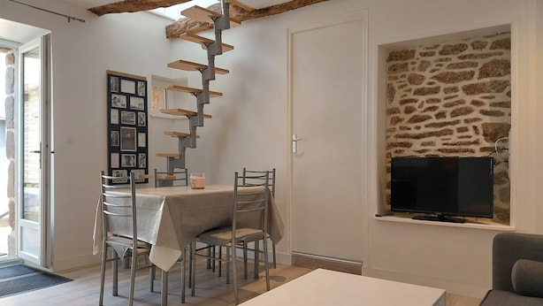 Ein Essbereich mit Tisch und Stühlen, einem Holzbodenregal, einer Steinwand mit Fernseher und einer Tür, die nach draußen führt.