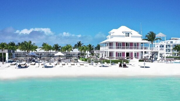 Um hotel na praia com várias varandas, área de piscina e um lounge à beira-mar.