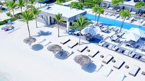 Vista aérea de um resort à beira-mar com espreguiçadeiras, guarda-sóis e uma piscina.
