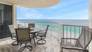 Un balcon avec une table et des chaises, donnant sur une plage et l’océan.