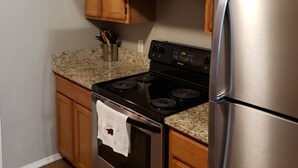 A kitchen with wooden cabinets, a stainless steel refrigerator, a black stove, and granite countertops. - Northwest Arkansas Adventures- Beautiful Condo, with Two Master Bedrooms   (Fayetteville)