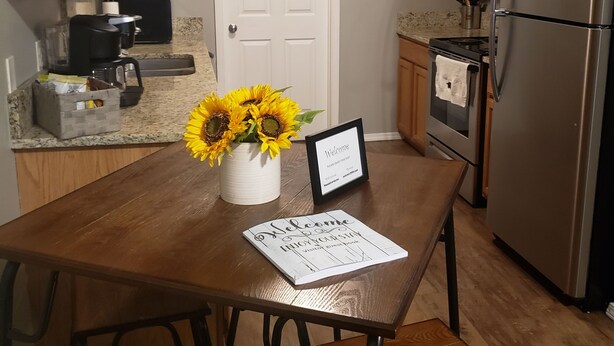 A kitchen with wooden cabinets, a stainless steel refrigerator, a coffee maker, and a welcome sign on the table. - Northwest Arkansas Adventures- Beautiful Condo, with Two Master Bedrooms   (Fayetteville)