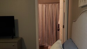 A bedroom with a bed, a TV on a dresser, and a door leading to a bathroom with striped curtains. - Northwest Arkansas Adventures- Beautiful Condo, with Two Master Bedrooms   (Fayetteville)