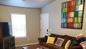 A living room with a brown leather couch, a wooden coffee table, a ceiling fan, and a colorful abstract painting on the wall. - Northwest Arkansas Adventures- Beautiful Condo, with Two Master Bedrooms   (Fayetteville)