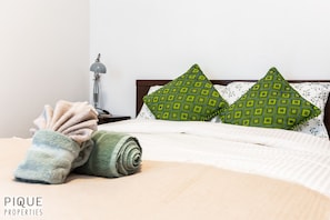 A neatly made bed with a rolled towel, two patterned pillows, and a lamp on a bedside table.