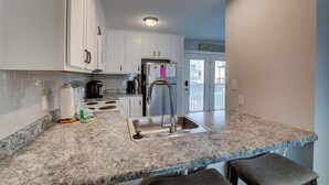 Una cocina moderna con gabinetes blancos, encimera de granito, pileta de acero inoxidable y un refrigerador.