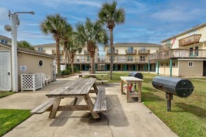 A courtyard with picnic tables, a barbecue grill, and a trash can. - Amazing 2BR Gulf View Condo | Private Beach Access (Gulf Shores)
