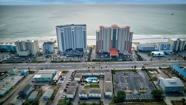 Vista aérea de una zona hotelera costera con varios edificios altos, un estacionamiento y una playa al fondo.