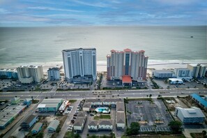 An aerial view of a coastal hotel area with multiple high-rise buildings, a parking lot, and a beach in the background. - Amazing 2BR Gulf View Condo | Private Beach Access (Gulf Shores)