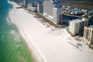 Un hotel frente al mar con varios edificios altos, una playa de arena y una piscina.
