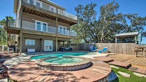 A two-story building with a backyard featuring a swimming pool, a hot tub, and a wooden deck. - Private Pool/Pier - Beautiful Bayfront Property! (Gulf Shores)