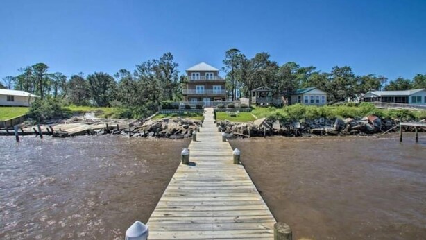 A wooden pier leading to a large house with a balcony, surrounded by trees and a clear sky. - Private Pool/Pier - Beautiful Bayfront Property! (Gulf Shores)