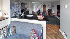 Eine moderne Küche mit schwarzem Tresen, einer Spüle und einem Korbwannenregal gefüllt mit Gegenständen. Eine Treppe führt in einen anderen Raum.