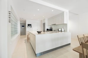 A modern kitchen with a central island, white cabinetry, and a dining area with wooden chairs.