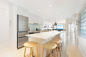 A modern kitchen with a large island, bar stools, and a view of the sea. - Luxury Stay – La Mer Noosa Apartment 09 (Noosa Heads)