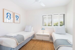 A bedroom with two beds, a nightstand, a lamp, and a window with blinds.