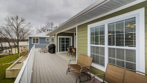A covered deck with outdoor furniture, a grill, and a view of a lake.