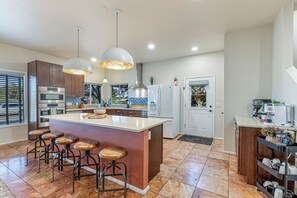 Cozinha moderna com ilha central, banquetas, eletrodomésticos de aço inoxidável e iluminação pendente.