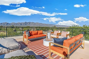 An outdoor seating area with a fire pit, sofas, and chairs, overlooking a mountainous landscape.