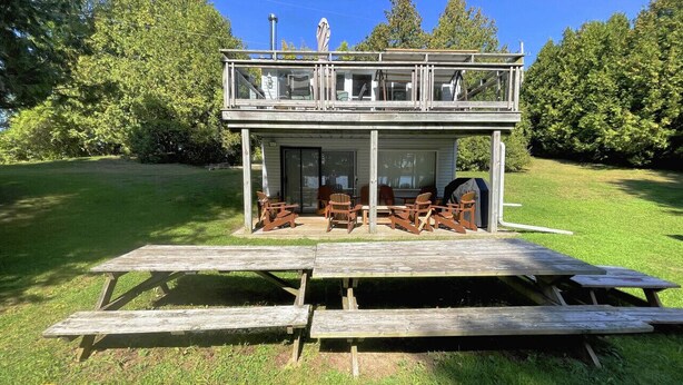 Estructura de madera de dos pisos con un porche cubierto y una mesa de picnic al frente.