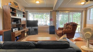 Una sala de estar con un sofá, un televisor, un mueble de entretenimiento de madera y un ventilador.