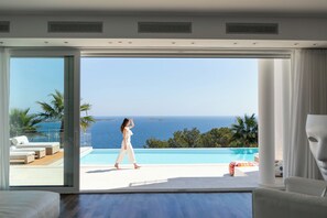 Een moderne kamer met een grote schuifglazen deur die leidt naar een balkon met zwembad en uitzicht op zee.