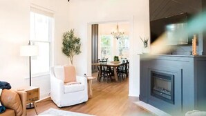 A modern living room with a fireplace, a dining area, and a large window. - The Oasis- Hot Tub+Fire Pit (Cincinnati)