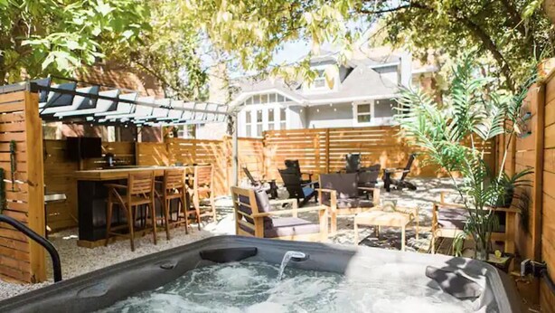 A hot tub in a backyard with wooden furniture and a fence. - The Oasis- Hot Tub+Fire Pit (Cincinnati)