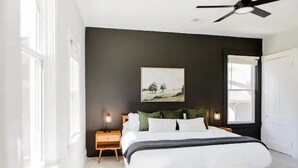 A modern bedroom with a large bed, bedside tables, a ceiling fan, and a window. - The Oasis- Hot Tub+Fire Pit (Cincinnati)
