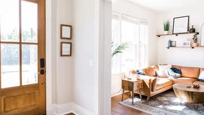 A bright living room with a wooden door, a sofa, a coffee table, and a rug. - The Oasis- Hot Tub+Fire Pit (Cincinnati)