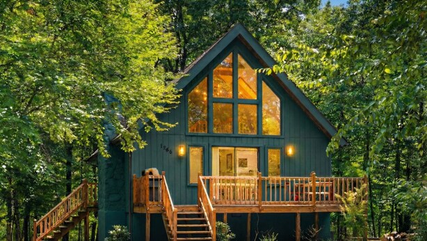 Een chalet met een houten terras, een trap en een groot raam.