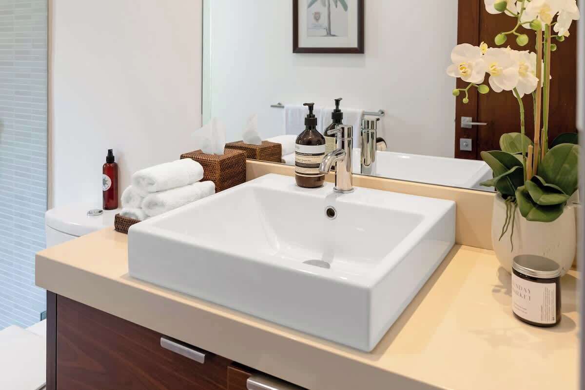 A bathroom with a white sink, a mirror, a bottle of soap, a towel, and a potted orchid.